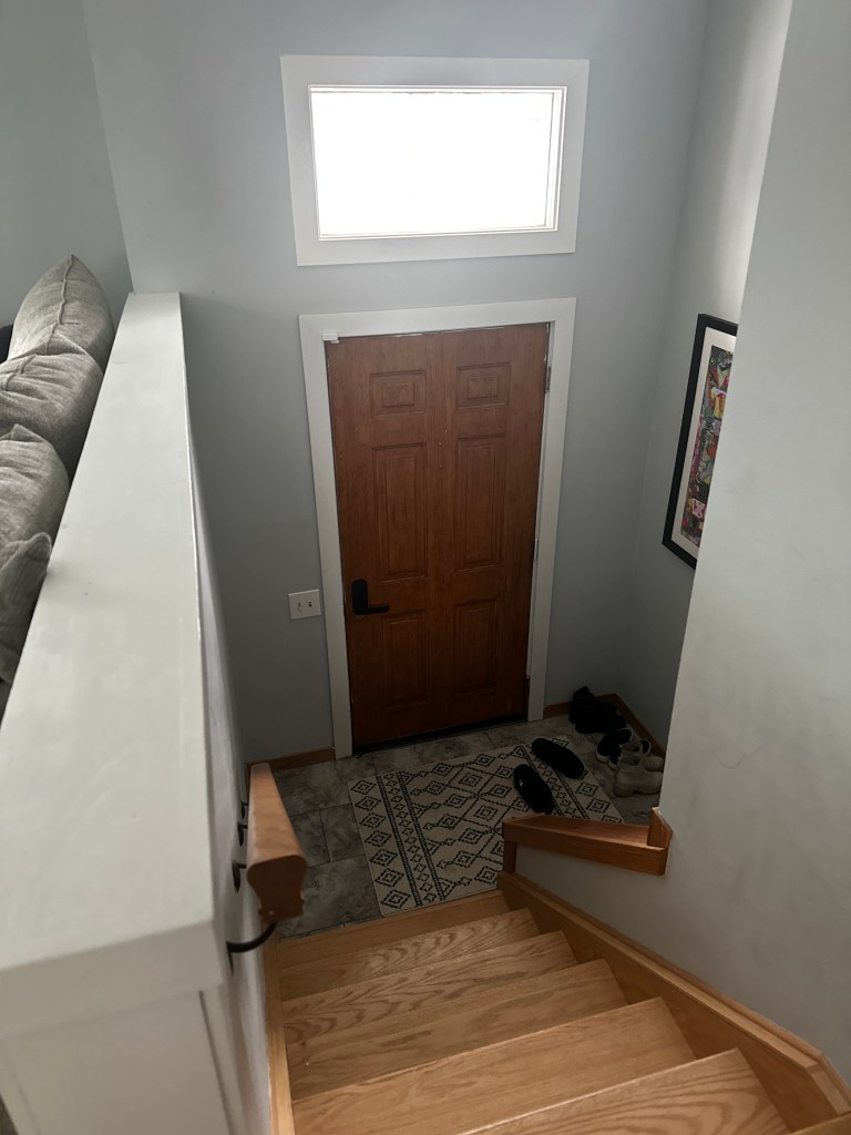 Interior view of the original solid front door with no glass panel, in a dark, narrow split-level entry landing, before the door was replaced