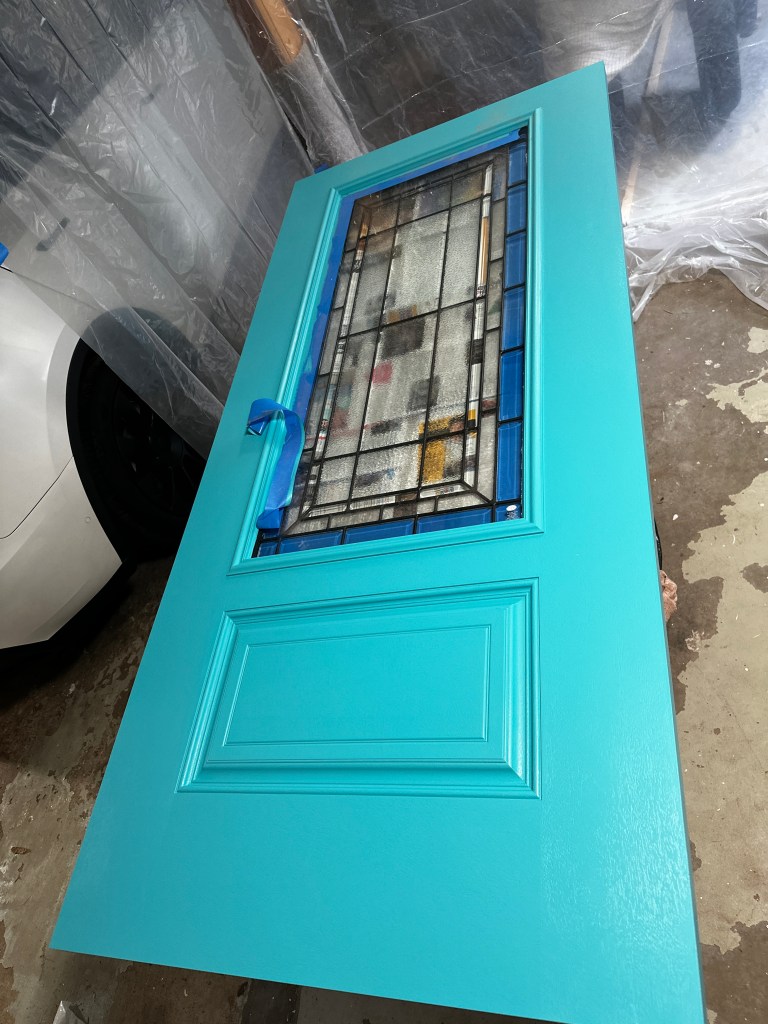 The new front door laid on sawhorses in the garage, being hand-painted a custom-mixed Behr teal